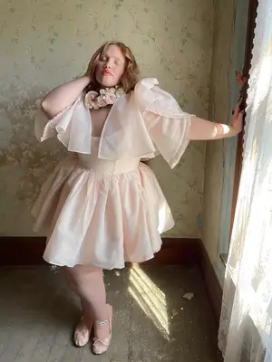 Model wearing light pink romantic mini dress and rose capelet paired with Miu Miu ballet flats