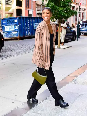 Gabrielle Union wears a pinstriped cardigan, black jumpsuit, platform heeled boots, and an olive green Aupen bag