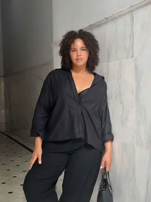 Woman wearing black button-down shirt, bra, tailored pants, and handbag