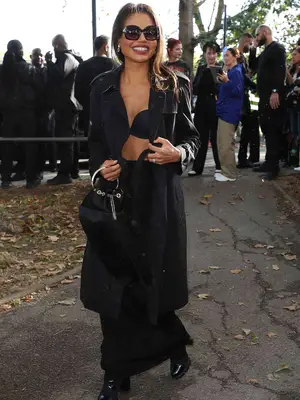 Woman wearing black outfit including trench coat, bra top, handle bag, and boots