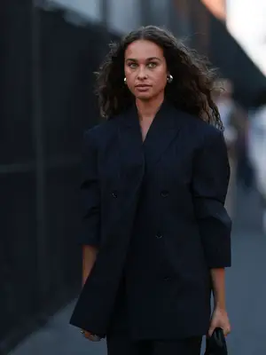 Woman wearing black pinstriped blazer, pants, and handbag with silver hoop earrings