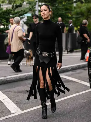 Woman wearing black turtleneck bodysuit and fringe skirt with belt and knee-high boots