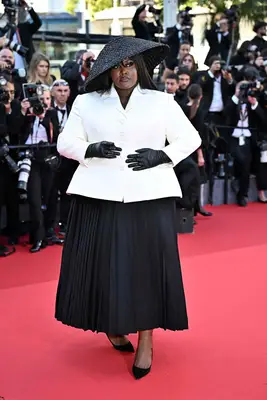Yseult wears a Dior jacket and skirt set with hat, leather gloves, and pointed-toe shoes at Cannes 2024