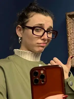 emma chamberlain taking mirror selfie with hair in bun and wearing bold rectangular eyeglasses
