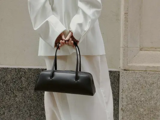 Close-up of woman wearing white outfit and carrying black east-west handbag