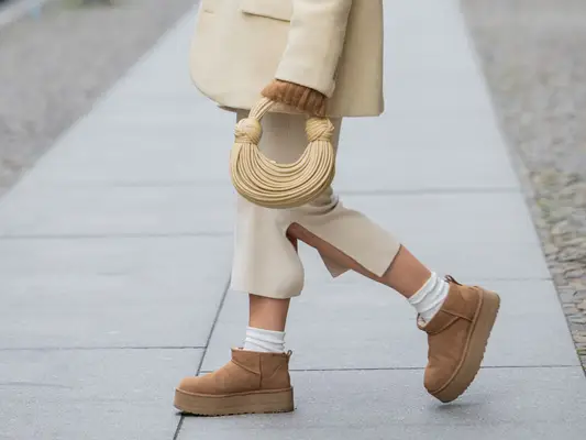 Person wearing chestnut brown Uggs with white socks and a cream-colored outfit. 