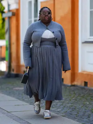 Abisola Omole wears a gray cardigan, pleated skirt, and gray suede sneakers
