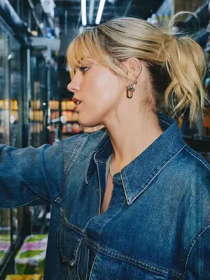 Renee Rapp wears a denim jumpsuit, updo hairstyle, and mixed metals earrings