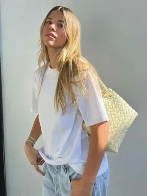Sofia Richie Grainge wears a white t-shirt, light wash jeans, woven off-white handbag, and layered mixed metals bracelets