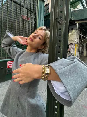 Woman wearing gray mini dress, silver watch, and gold chain bracelet