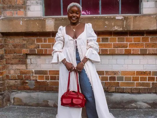 Tatenda Luna wears an open buttoned maxi dress, wide leg jeans, layered necklaces, and red handbag