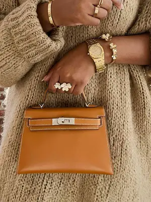 Close-up of woman wearing sweater dress and gold jewelry and carrying an Hermes Kelly bag