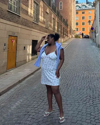 Woman wearing a patterned mini dress with blue cardigan over shoulders and white flip flops