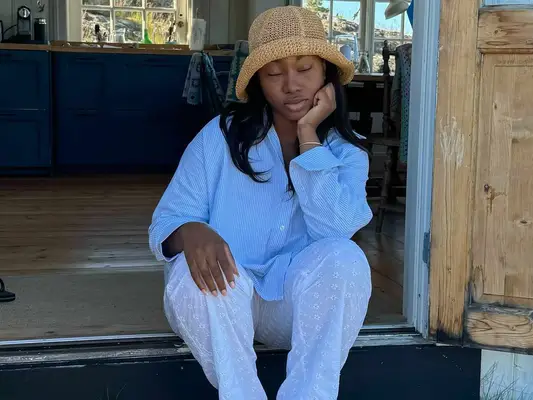 Nnenna Echem wearing blue striped button-down with eyelet white pants and a raffia hat