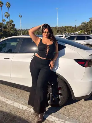 Bella Golden wears a black corset, black denim flare jeans, and silver hoop earrings 