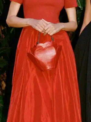 Close-up of woman carrying Staud rose Juliet bag and wearing red dress