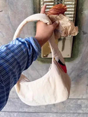Close-up of person carrying Baggu swan bag and croissant