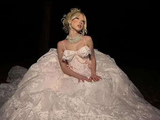 Woman wearing voluminous powder pink gown with lace embroidery, ruffles, and strands of pearls