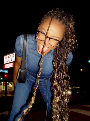 Alyah Chanelle Scott wears a denim shirt, jeans, black shoulder bag, and eyeglasses