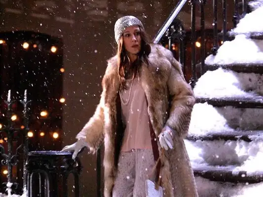 Sarah Jessica Parker as Carrie Bradshaw wears sparkly hat, fur coat, white shirt, floral pants, white pearls, gloves, and booties