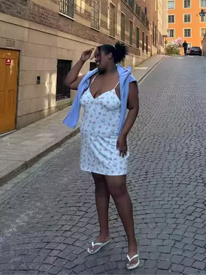 Close up of a model wearing a Djerf Avenue assorted fruit print slip dress and white flip flops.