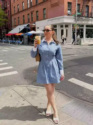 MYM Beauty writer Claire Brodsky wears a striped shirt dress, open-toed white heels, brown handbag, sunglasses, and ponytail hairstyle
