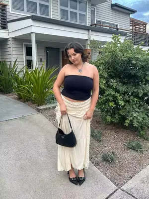 Woman wearing tube top, ruched maxi skirt, black pointed-toe flats, Prada handbag, and necklace