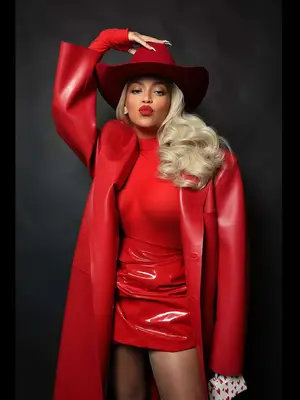 Beyonce wears a red turtleneck, patent leather mini skirt, leather trench coat, and cowboy hat