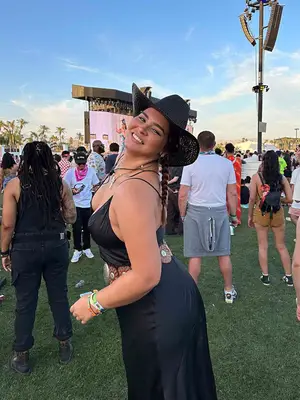 Bella Golden wears a black slip dress, studded belt, black cowboy hat, and layered jewelry