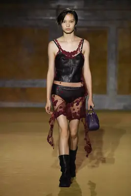 A model wears a leather crop top, bloomers, and a sheer overlay dress with red embroidery at the Coach Spring 2024 show