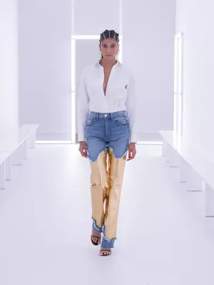 A model wears a white tailored shirt, jeans with gold brushed metallic paneling, and silver knotted earrings on the Brandon Maxwell spring 2024 runway