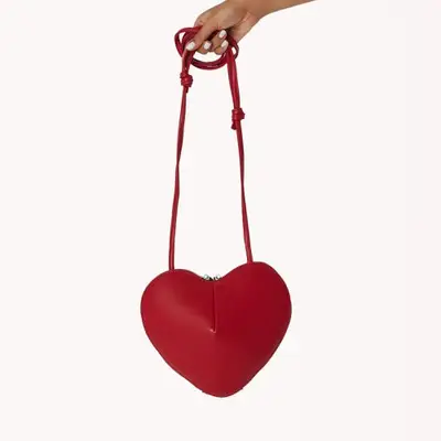 hand holding red heart shaped bag with long shoulder strap