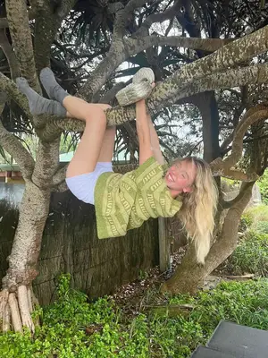 Sydney Sweeney wearing a pair of gray micro shorts, gray socks, and a green striped shirt while hanging from tree