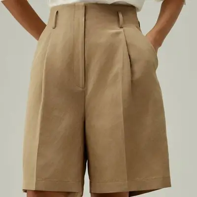 Model wearing beige tailored Bermuda shorts 