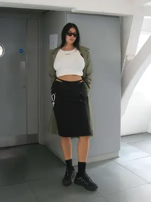 Lauren Chan wearing a white cropped top with a black cargo midi skirt, sunglasses, and an olive green jacket