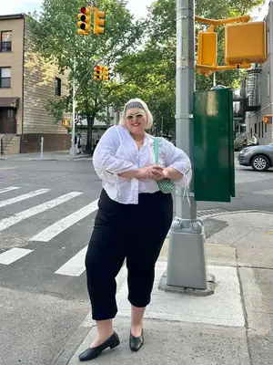 Influencer, @theabbybible is standing outside wearing a white button down shirt, black capris, and a gingham headband. 