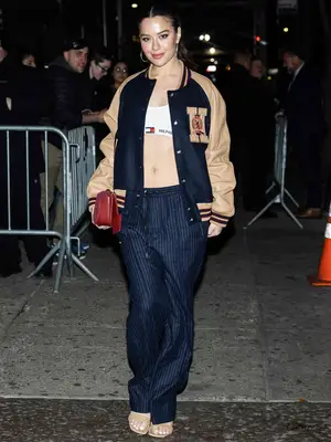 Tessa Brooks wears a Tommy Hilfiger varsity jacket, sports bra, pinstripe pants, sandals, and red bag