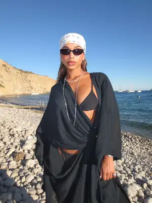 Lori Harvey wearing a black bikini, swimsuit cover-up, and layered necklace