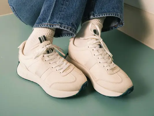 Close-up of person wearing white and green sneakers with foam/gum soles and jeans