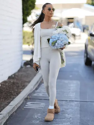 Jasmine Tookes wearing a cream athleisure set with a cardigan and sand colored, short Ugg boots.
