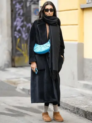 Woman wearing an oversized gray coat with black leggings and mini chestnut Uggs.