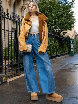 Woman wearing light wash wide leg denim, a suede jacket, and platform Ugg boots.