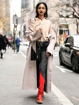 Woman wearing knit polo, trench coat, knit skirt, red tights and boots, and black handbag