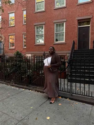 Abisola Omole wears a white tee, brown cardigan and rib knit skirt, two-tone slingback shoes, and black crossbody bag
