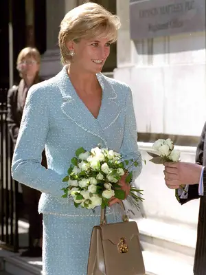 Princess Diana wearing a blue tweed skirt suit holding white flowers and tan Lana Marks Princess Diana bag