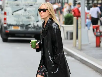 Chloe Sevigny wears a black vinyl jacket, floral mini dress, and sunglasses while carrying a green matcha
