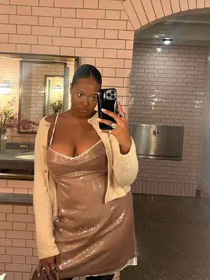 Imani Randolph wears a bronze sparkly slip dress and beige buttoned cardigan while taking a mirror selfie