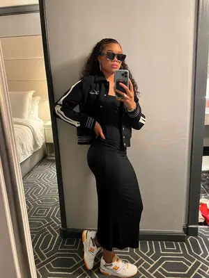 Storm Reid wearing a black maxi dress, white sneakers, black athletic jacket, and sunglasses