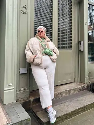 Abby Bible wearing a beige puffer jacket, green patterned top, green crossbody bag, sweatpants, beret, and New Balance sneakers