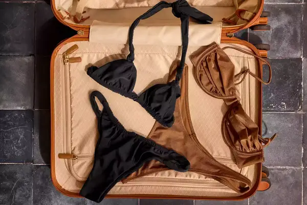 Open suitcase with black and brown swimsuits laid inside